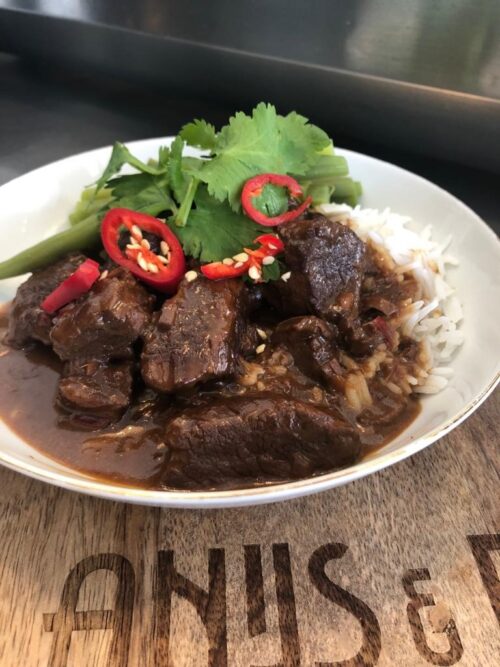 Rendang van rund met witte rijst en komkommer en rode ui op het zuur