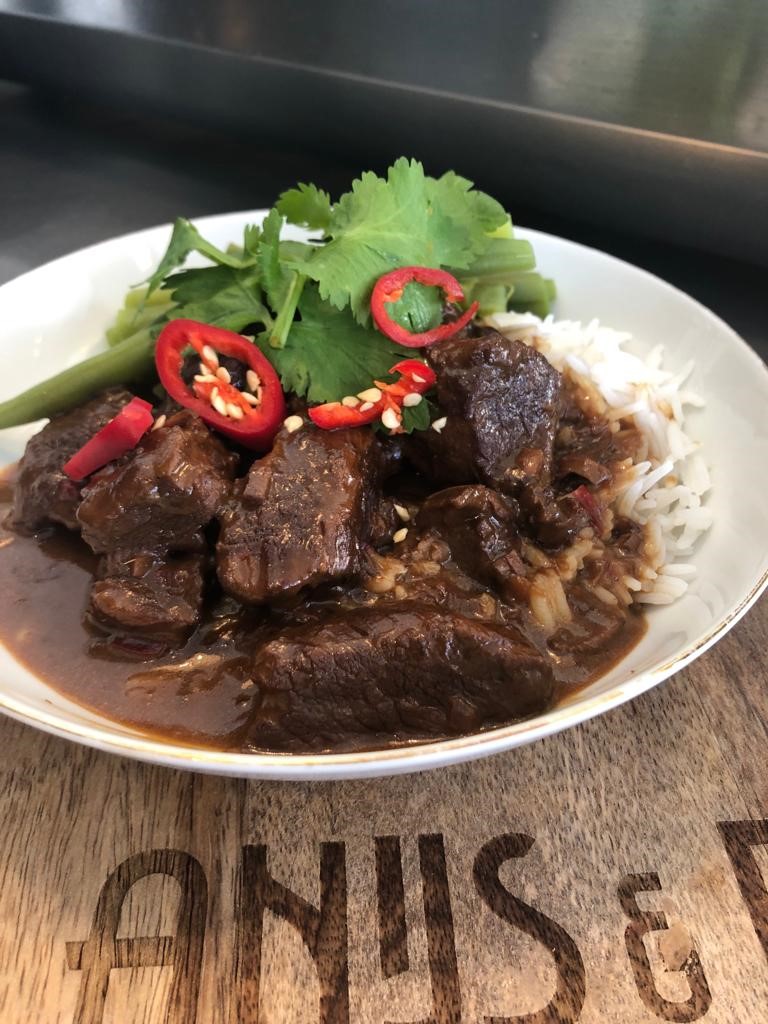 Rendang van rund met witte rijst en komkommer en rode ui op het zuur